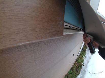 vinyl siding pulled away from the wall exposing the top of the lower piece of siding