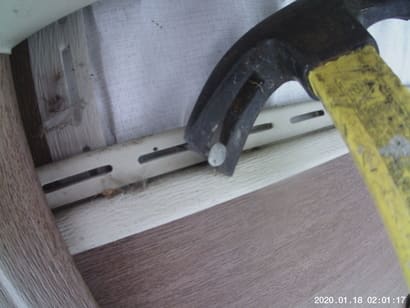 pulling nails from the top of vinyl siding with a hammer