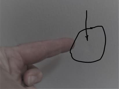 photo of a finger pointing at a drywall dent