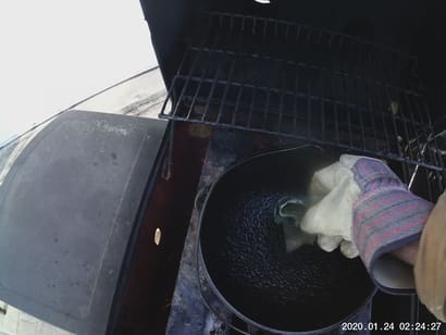 photo of a hand in a glove coating chicken fat on a cast iron pot for second seasoning